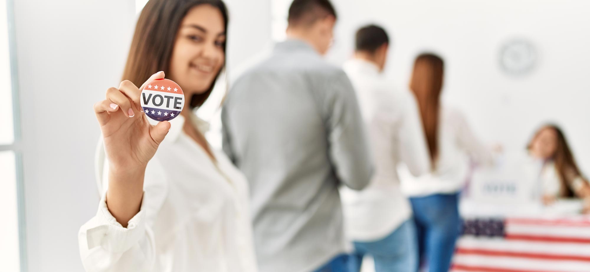 Woman holding a VOTE button at a polling place